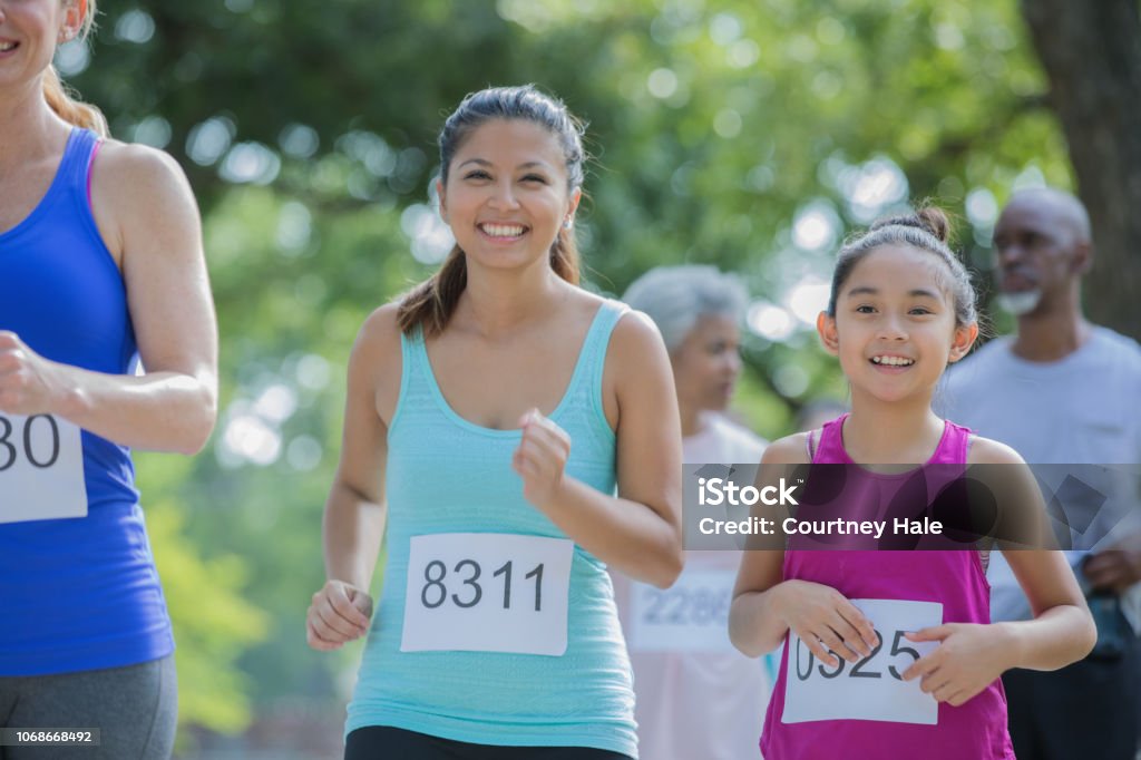 Asian mother and daughter run together in a marathon Asian mother and daughter run together in a marathon. They are smiling.  They are in a public park on a sunny day. Marathon Stock Photo