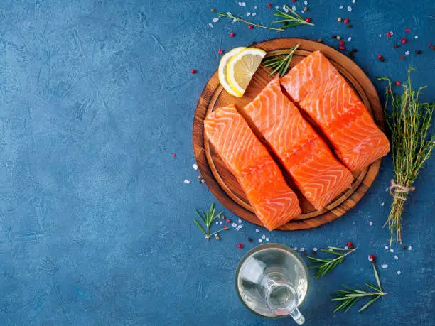 Food background, sliced portions large salmon fillet steaks on chopping board on dark blue concrete table, copy space, top view.