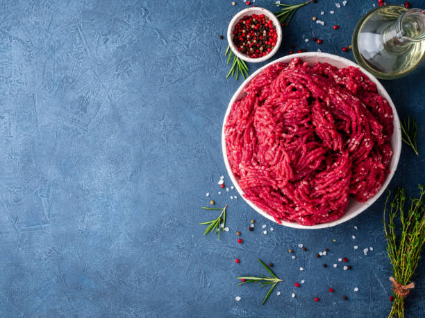 Mince beef, ground meat with ingredients for cooking on dark blue background with copy space, top view