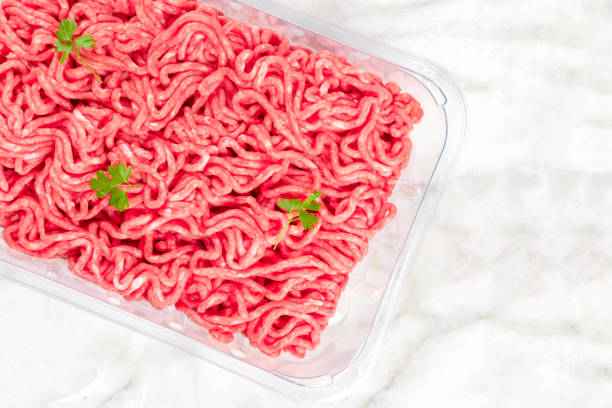 eine obenliegende foto von hackfleisch / faschiertem in einem plastikbehälter, erschossen von der spitze auf weißem marmor hintergrund mit petersilie und einem platz für text - veal raw meat pink stock-fotos und bilder