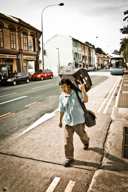 ein ausländischer arbeitnehmer trägt sein gepäck auf der straße - editorial asia singapore tourist stock-fotos und bilder