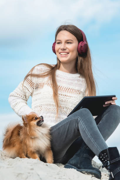 niña de 14 años en un auriculares escuchando una música de un teléfono inteligente en una playa. contra un cielo azul. cierre para arriba - pampered pets audio fotografías e imágenes de stock