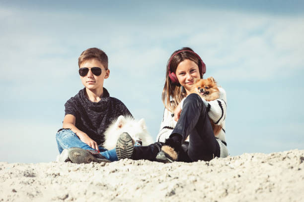 garçon de 11 ans heureux étreindre son chien de race samoyède au bord de la mer avec un ciel bleu se bouchent. meilleurs amis reste et de s’amuser en vacances, de jouer dans le sable - pets water lake sky photos et images de collection