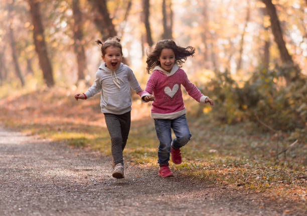 two irresistibly cute little girls run side by side and hold hands in a sunny autumn day. Two sisters are having fun and running out. In the autumn landscape of two girls having fun in running.