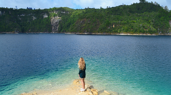 Blond young girl standing in front of blue lagoon in Chiapas, Mexico