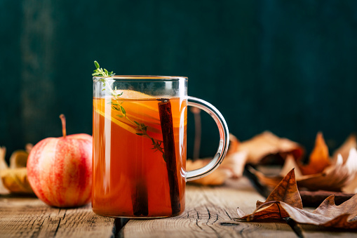 Apple tea with cinnamon, warming drink, old wooden background, fallen leaves
