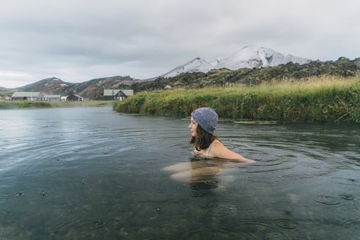Young Caucasian woman resting in hot natural pool in Iceland