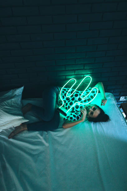 Under the neon light Young woman lying down on a bed in bedroom under the green neon light of cactus lamp neon bedroom stock pictures, royalty-free photos & images