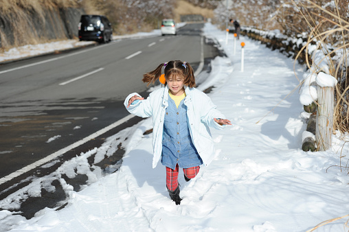 Beautiful little girl mixed race Japanese and Brazilian running happy beside the road after snowfall. Shizuoka Prefecture, Japan. Winter of February 2011.
