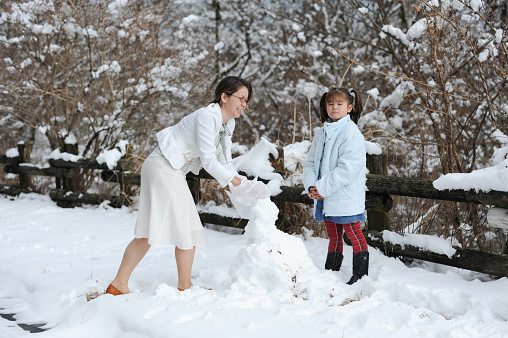 Young and beautiful mother smiling and her little daughter looking indifferent at the camera. Making a snowman together. Shizuoka Prefecture, Japan. Winter of February 2011.