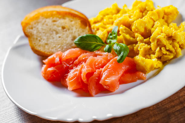 istock Scrambled eggs with smoked salmon and toast in white plate on wooden table background 1068747848