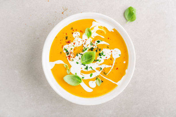 Pumpkin creamy soup served in bowl Tasty appetizing pumpkin vegetable creamy soup decorated with basil, cream and spices served in white bowl on grey table. View from above. Horizontal. pumpkin soup photos stock pictures, royalty-free photos & images