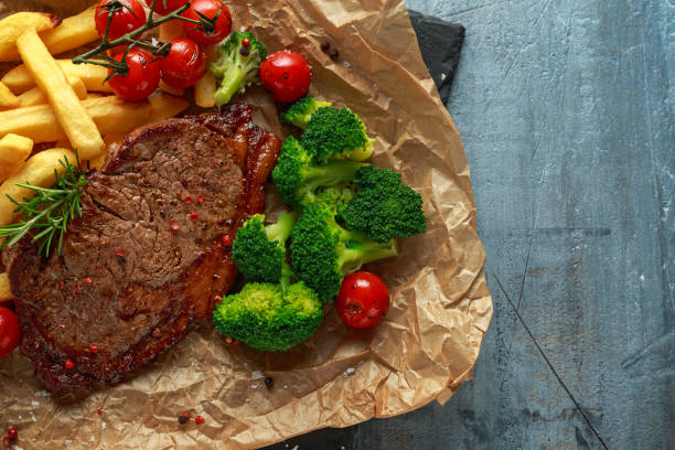 Grilled sirloin steak with potato fries, broccoli and cherry tomatoes on crumpled paper