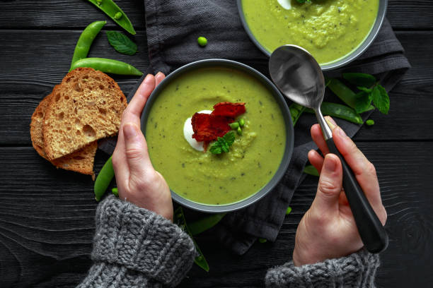 istock Hands in sweater, pullover holding cosy warming in cold weather. Sweet pea, leek and mint hot soup topped with crunchy bacon and dolop of yogurt 1068756762