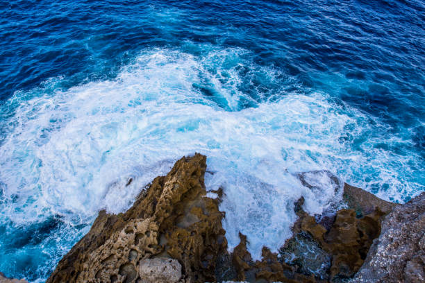 This pic shows aerial view big blue sea waves crashing the coast and sea rocks. The pic is taken by drone in Indonesia and from top. The sea waves are captured when they hit the sea coastlines.