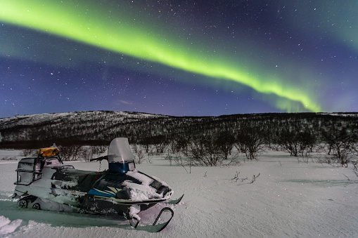 Beautiful green northern lights and snowmobile on foreground, Norway