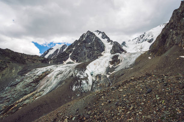 istock Snowy giant mountain range under cloudy sky. Rocky ridge with snow. Huge glacier. Icy mountainside with water streams. Wonderful mountains. Atmospheric minimalist mountainous landscape of nature. 1068788850