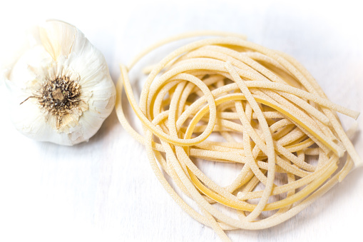 Nest of Raw Linguini and Garlic, White Background Overhead. Copy space available.