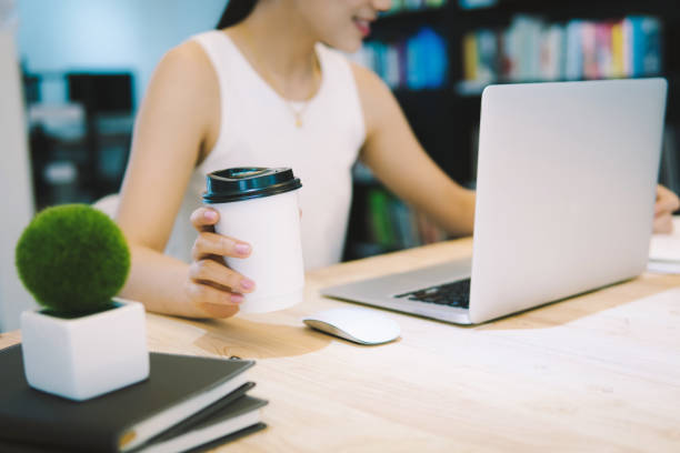 istock Business woman drinking coffee and working taking notes ideas new project in notebook with laptop at office desk. 1068815446