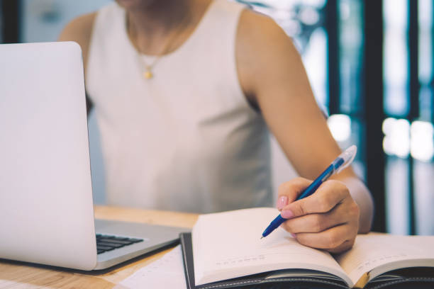 istock Business woman taking notes in notebook for working financial chart with a laptop at office desk. 1068817268
