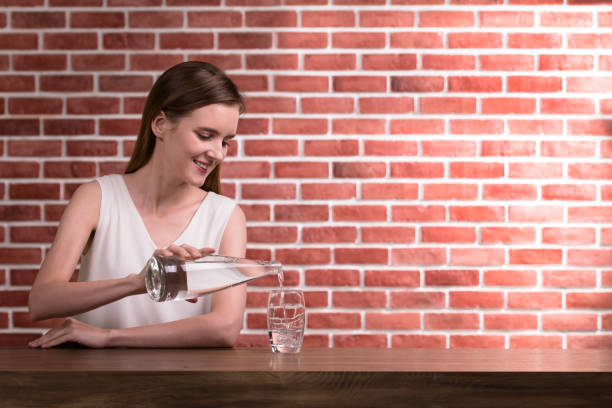 Young woman pouring water from bottle into glass in the room