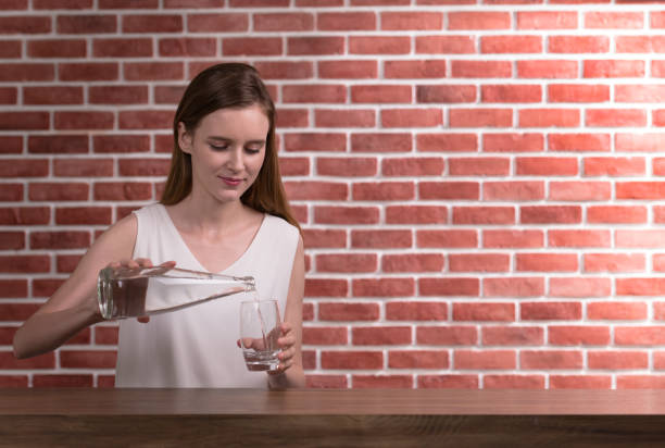 Young woman pouring water from bottle into glass in the room