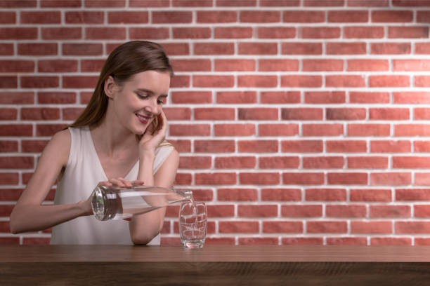 Young woman pouring water from bottle into glass in the room