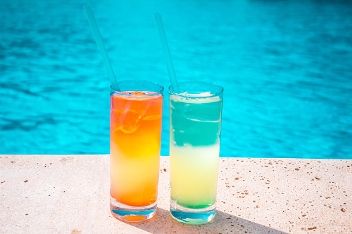 Two colorful tropical cocktails on the background of the pool. Exotic summer holidays. Color cocktails on the background of water.