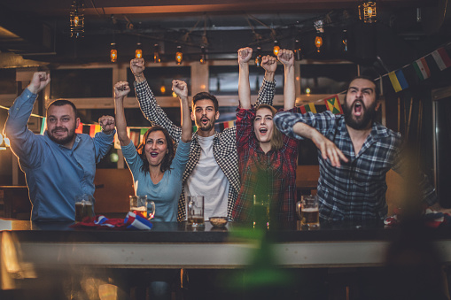 Group of young people, celebrating in a pub all together, watching a sports game.