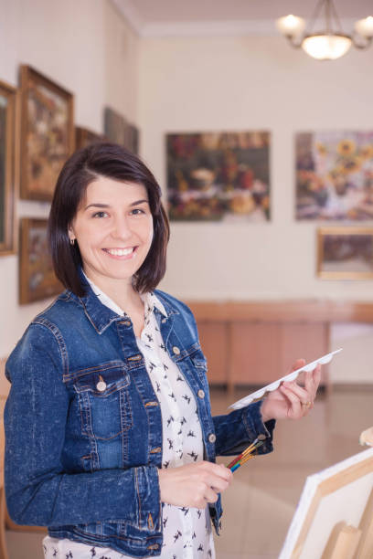 istock Cute young woman painting a picture near an easel in a studio. 1068856484