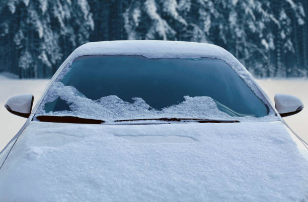 雪に覆われた森林の背景に前面フロント ガラスとボンネットを見る雪の覆われた自動車を凍結、 - frozen windshield cold car ストックフォトと画像