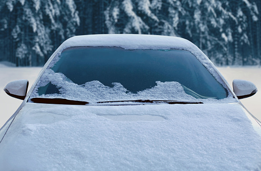 Frozen winter car covered snow, view front window windshield and hood on snowy forest background