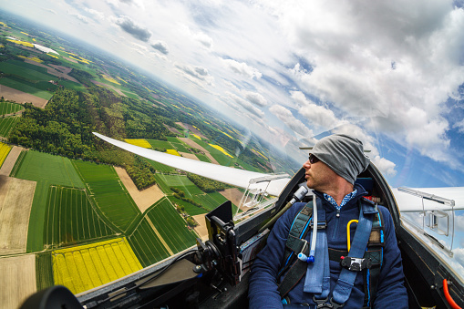 View of the pilot in the cockpit of a glider in flight over fields as an aerial photograph