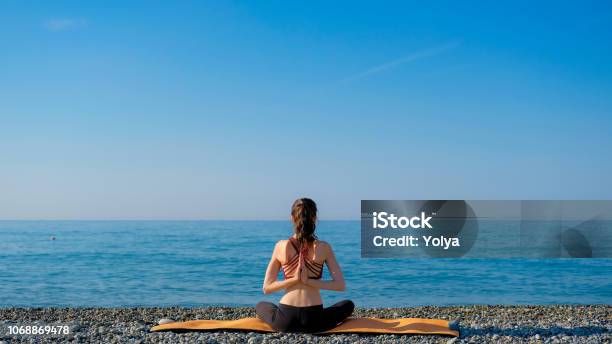 Young Slim Woman In Tight Sportswear Sitting On Orange Yoga Mat And  Practicing Outdoors At Pebble