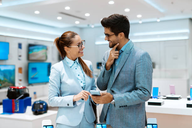 istock Happy couple dressed in business clothes choosing new smart phone while standing in tech store. 1068874092