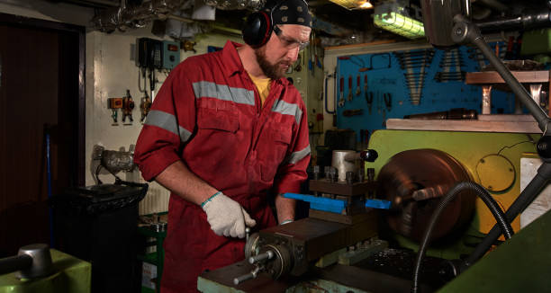istock Worker in red uniform operating in manual lathe in metal big workshop. 1068879700