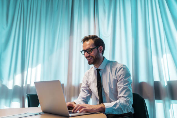 istock Smiling businessman using laptop while sitting in office. Hands on keyboard. In background curtain. 1068881536