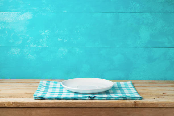 Empty white plate on wooden table with tablecloth over blue background
