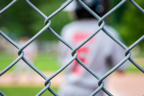 Play ball, junior youth league baseball player viewed from behind through the chain link fence while standing ready in batters box, background, concept.
