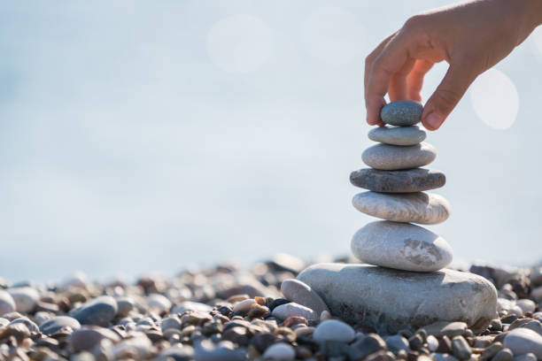 main d’enfant équilibrage pile de pierres sur la plage - balancing stones photos et images de collection