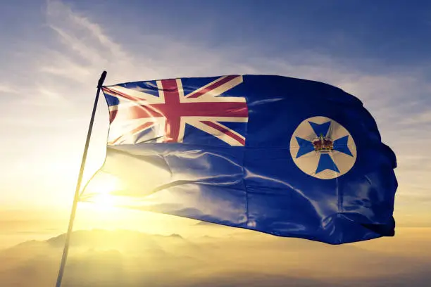 Photo of Queensland state of Australia flag textile cloth fabric waving on the top sunrise mist fog