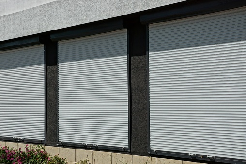 three large windows covered with white plastic shutters on the wall of the building