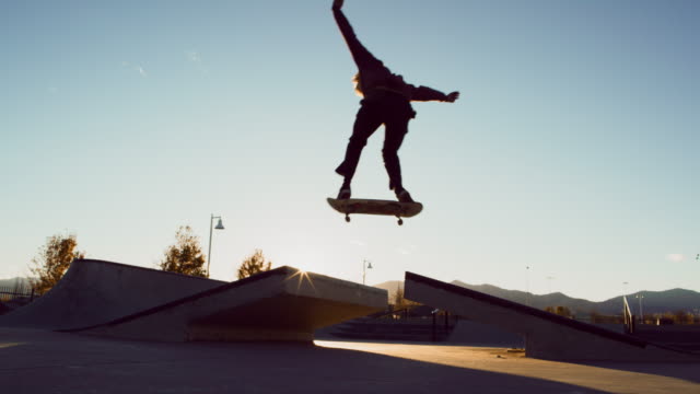 A Teenaged Caucasian Boy Performs a Regular Foot Ollie Over a Gap with His Skateboard at the Skatepark