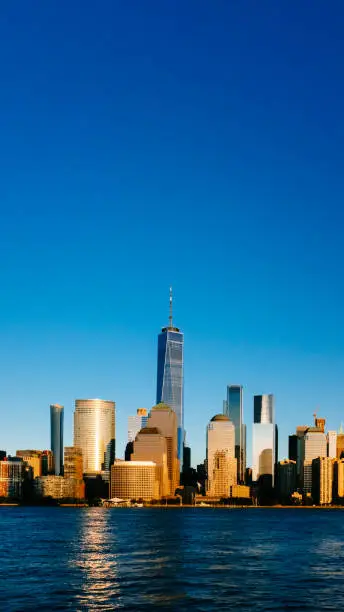 Photo of Skyline of downtown Manhattan over Hudson River under blue sky, at sunset, in New York City, USA