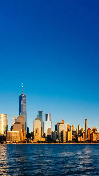 Photo of Skyline of downtown Manhattan over Hudson River under blue sky, at sunset, in New York City, USA