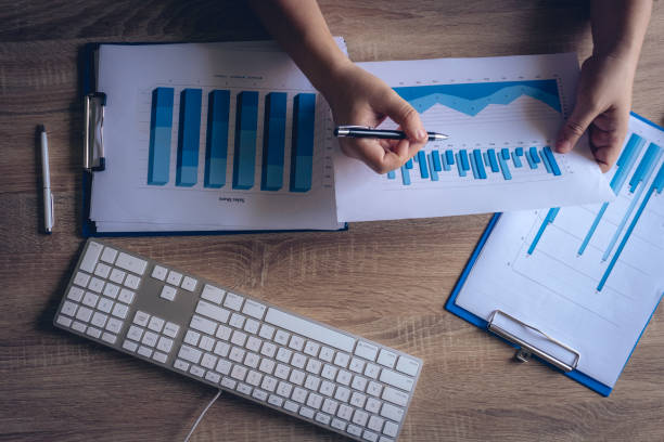 istock Modern Office working desk table, The business hands uses chart or graph for checking  finance with keyboard,notebook ,pen, eyeglasses.Top view background for copy space. 1069015912