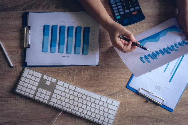 istock Modern Office working desk table, The business hands uses calculator for checking chart and graph finance with keyboard,notebook ,pen, eyeglasses.Top view background for copy space. 1069016004