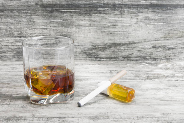 istock Not a full glass of alcoholic whiskey drink with an e-cigarette on a marble surface.Bad habits harmful to health 1069034320