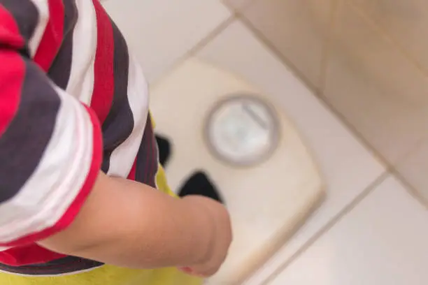 Photo of The child stands on the floor scales in a striped T-shirt, the view from the top. Health