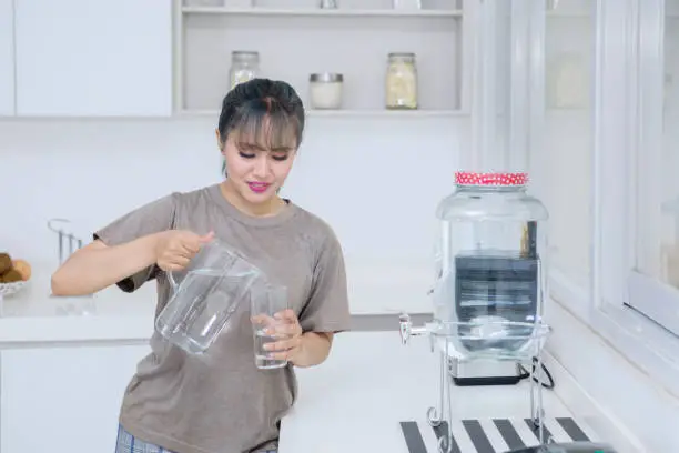 Picture of pretty girl pouring fresh water into the glass while standing in the kitchen room